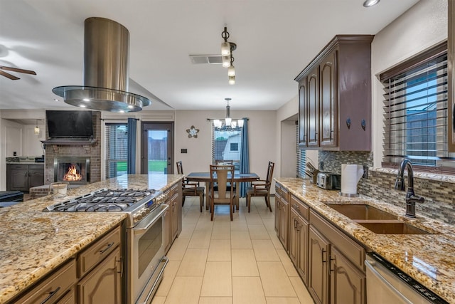 kitchen featuring appliances with stainless steel finishes, backsplash, a sink, a ceiling fan, and a brick fireplace
