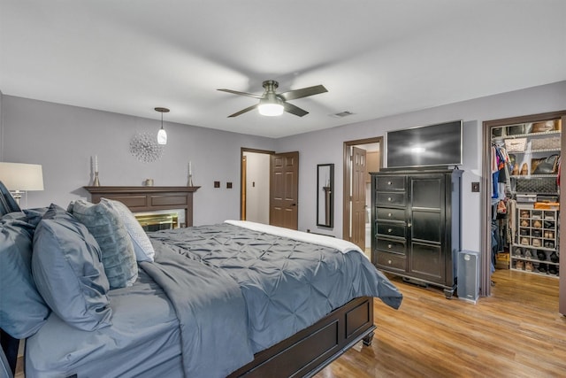 bedroom with a spacious closet, light wood-type flooring, a closet, and a ceiling fan