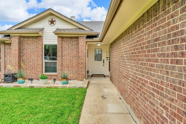 property entrance with brick siding, a shingled roof, and a yard