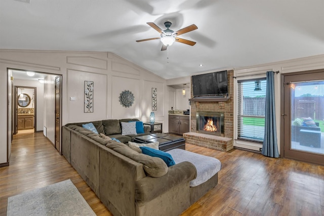 living room featuring vaulted ceiling, ceiling fan, a fireplace, wood finished floors, and a decorative wall