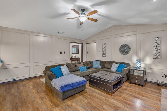 living room featuring a decorative wall, a ceiling fan, vaulted ceiling, and wood finished floors
