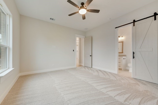 unfurnished bedroom featuring a barn door, light carpet, and multiple windows