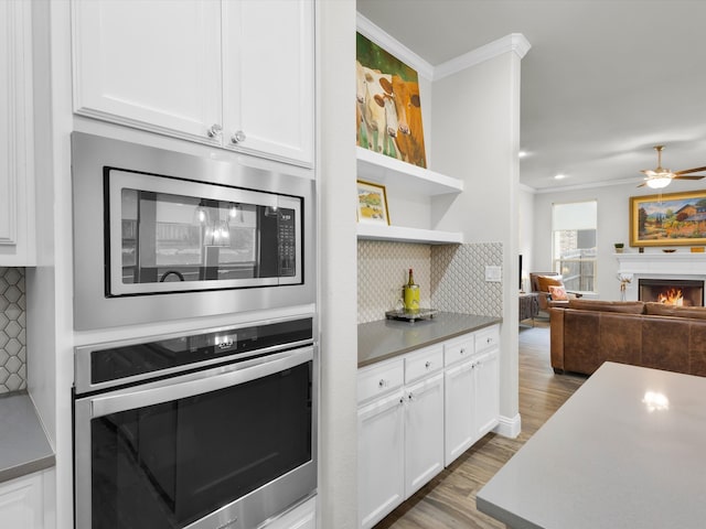 2209 Trace Ridge Dr, Weatherford, TX 76087 - kitchen featuring stainless steel appliances, ornamental molding, a lit fireplace, white cabinetry, and tasteful backsplash