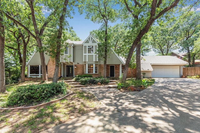 tudor-style house featuring brick siding, driveway, stucco siding, an attached garage, and fence