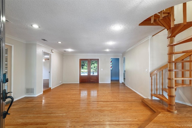 entrance foyer featuring a textured ceiling, light wood-style floors, french doors, crown molding, and stairway