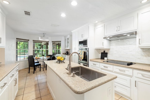 kitchen featuring stainless steel appliances, under cabinet range hood, an island with sink, a sink, and backsplash