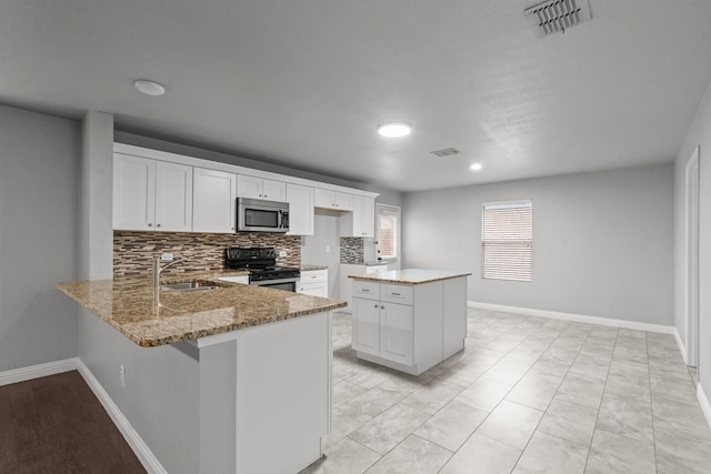 2720 Ocaso Dr, Little Elm, TX 75068 - kitchen featuring appliances with stainless steel finishes, light stone countertops, a peninsula, backsplash, and recessed lighting