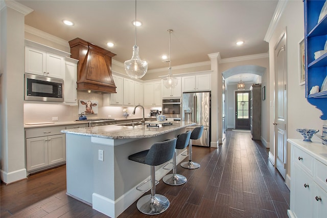 2700 Tremont Blvd, Mckinney, TX 75071 - kitchen with appliances with stainless steel finishes, arched walkways, crown molding, custom exhaust hood, and a breakfast bar