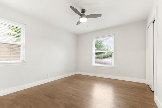 unfurnished bedroom with multiple windows, wood finished floors, baseboards, and a closet