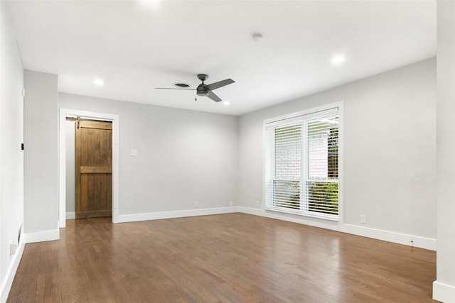 empty room featuring wood finished floors, ceiling fan, baseboards, recessed lighting, and a barn door