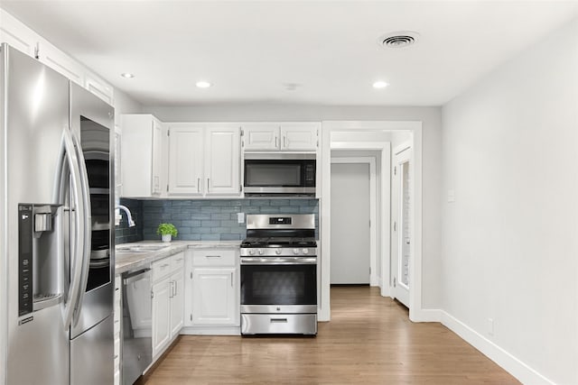 kitchen featuring stainless steel appliances, a sink, white cabinetry, decorative backsplash, and recessed lighting
