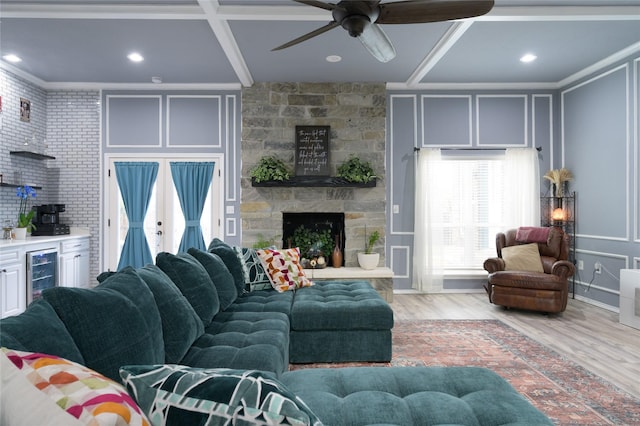 living area with a decorative wall, beverage cooler, light wood-style flooring, ceiling fan, and a stone fireplace