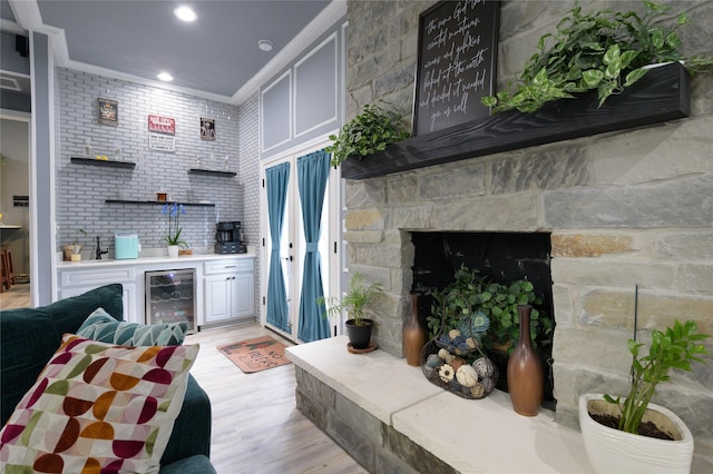 indoor bar featuring wine cooler, crown molding, light wood-style floors, a stone fireplace, and recessed lighting