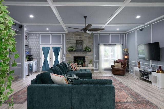 living room with coffered ceiling, a decorative wall, a fireplace, ceiling fan, and light wood-style floors