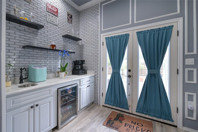 indoor bar with beverage cooler, french doors, ornamental molding, and light wood-style floors