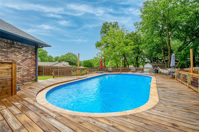 view of swimming pool with a wooden deck, a fenced backyard, and view of wooded area