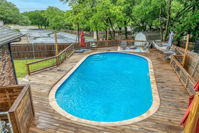 view of swimming pool featuring a deck, a storage shed, a fenced backyard, and an outdoor structure