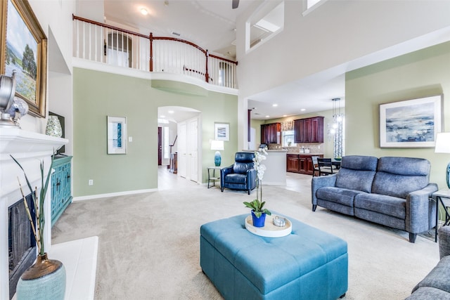 living area featuring light colored carpet, arched walkways, a fireplace, a high ceiling, and baseboards