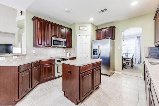 kitchen featuring stainless steel appliances, arched walkways, light countertops, a kitchen island, and decorative backsplash