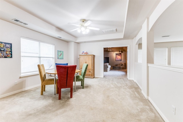 dining area featuring arched walkways, light carpet, a ceiling fan, a tray ceiling, and baseboards