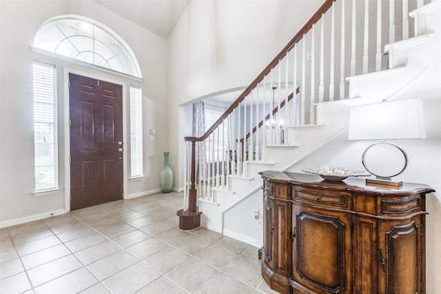 entrance foyer featuring light tile patterned floors, stairway, baseboards, and a high ceiling