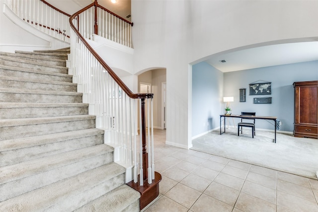 staircase with arched walkways, carpet, tile patterned flooring, baseboards, and a high ceiling