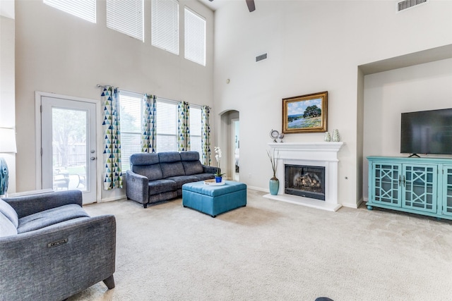 carpeted living room with plenty of natural light, a high ceiling, ceiling fan, arched walkways, and a fireplace with raised hearth