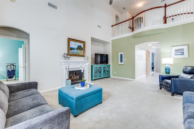 carpeted living room featuring arched walkways, a high ceiling, a fireplace, and baseboards