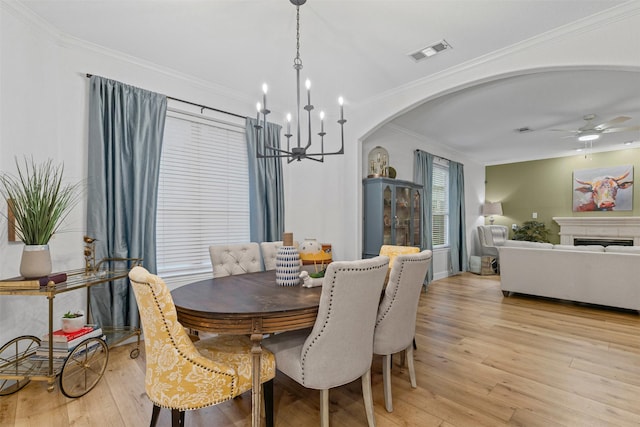 dining area featuring arched walkways, a chandelier, ornamental molding, light wood-style flooring, and a ceiling fan