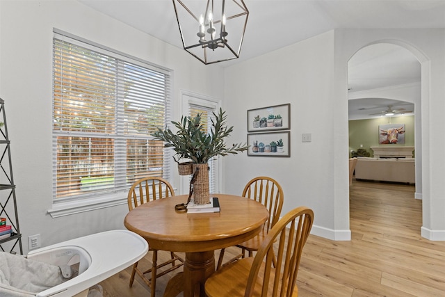 dining area with arched walkways, light wood finished floors, a chandelier, baseboards, and ceiling fan