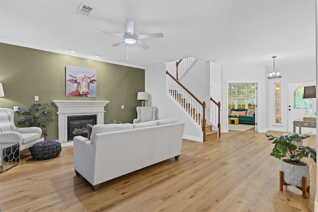 living room with stairway, light wood-style flooring, a glass covered fireplace, a ceiling fan, and baseboards