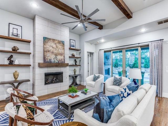 living room with wood finished floors, ceiling fan, beamed ceiling, baseboards, and a tiled fireplace