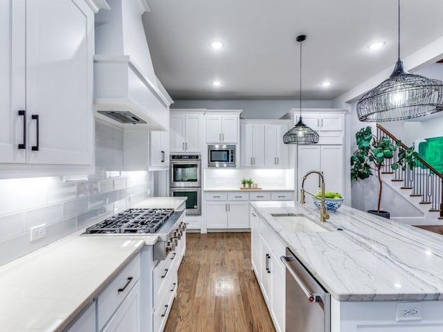 kitchen with stainless steel appliances, a sink, custom range hood, an island with sink, and backsplash