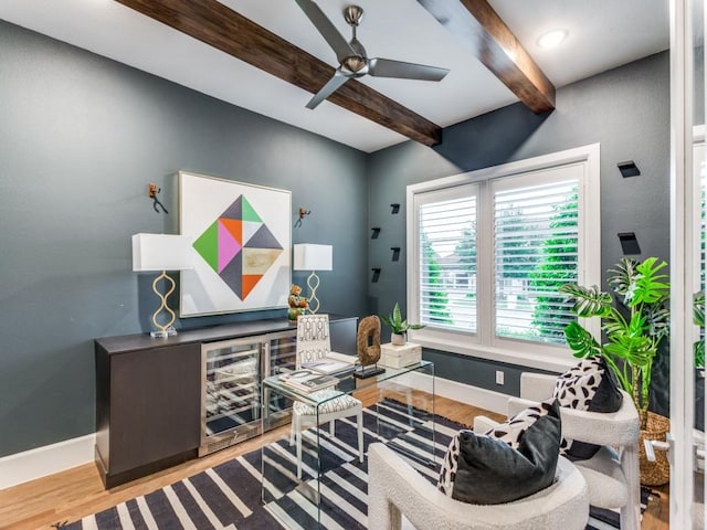 living area with beam ceiling, wood finished floors, baseboards, ceiling fan, and a dry bar