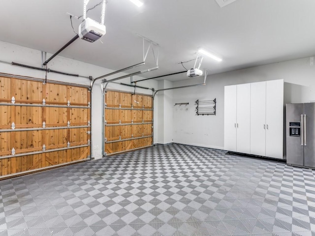garage featuring stainless steel fridge, a garage door opener, and baseboards