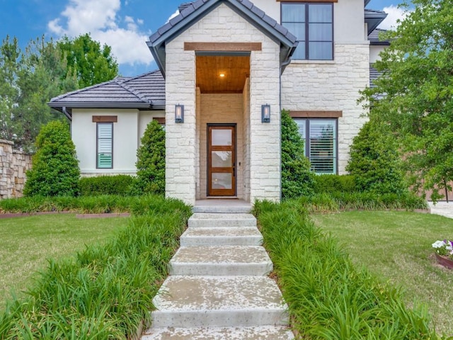 property entrance featuring stone siding, a lawn, stucco siding, and a tile roof