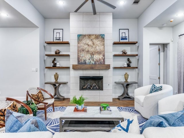 living room with a tiled fireplace, ceiling fan, wood finished floors, and baseboards