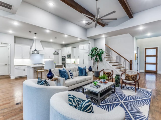 living room featuring light wood-style floors, a ceiling fan, beamed ceiling, recessed lighting, and stairs