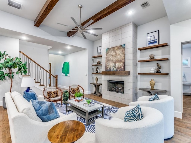 living area with light wood-style flooring, a ceiling fan, baseboards, a tile fireplace, and beam ceiling
