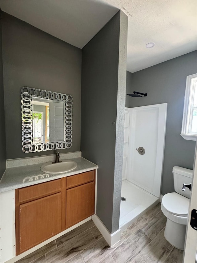 bathroom with a stall shower, toilet, wood finished floors, and vanity