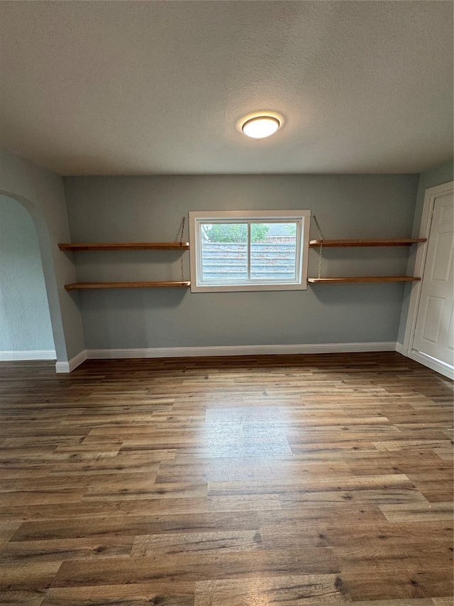 empty room with dark wood-style floors, arched walkways, a textured ceiling, and baseboards