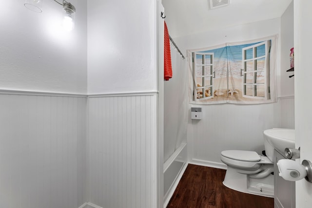full bathroom with a wainscoted wall, wood finished floors, toilet, and shower / bath combination with curtain