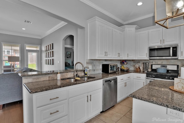 kitchen featuring appliances with stainless steel finishes, a sink, white cabinets, arched walkways, and dark stone counters