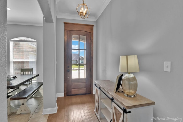 entryway with crown molding, a chandelier, light wood-style flooring, and baseboards