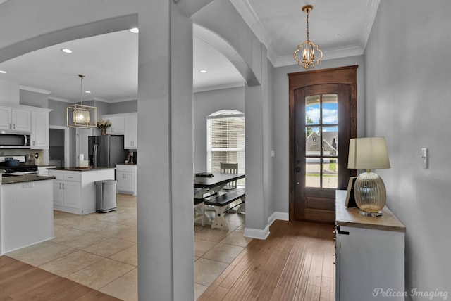 entrance foyer featuring a chandelier, arched walkways, ornamental molding, recessed lighting, and light wood finished floors