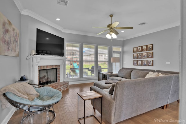 living area with a ceiling fan, a fireplace, crown molding, recessed lighting, and wood finished floors