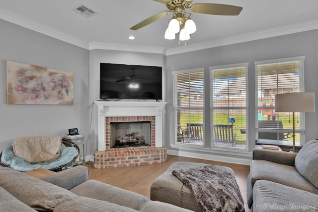 living area featuring a ceiling fan, healthy amount of natural light, a fireplace, wood finished floors, and crown molding