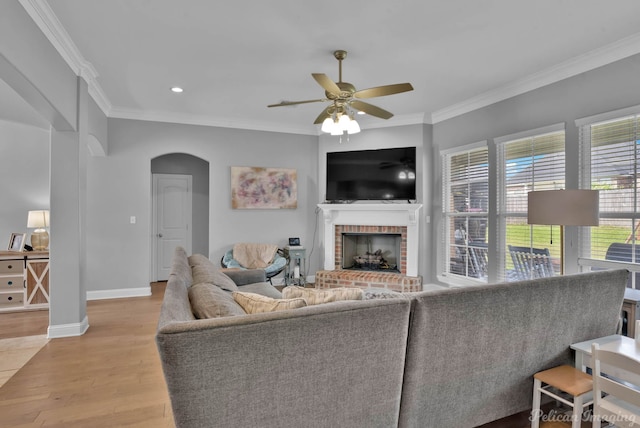 living room with arched walkways, a ceiling fan, ornamental molding, a fireplace, and wood finished floors