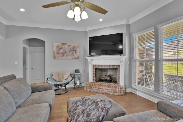 living area with ceiling fan, wood finished floors, a fireplace, arched walkways, and ornamental molding