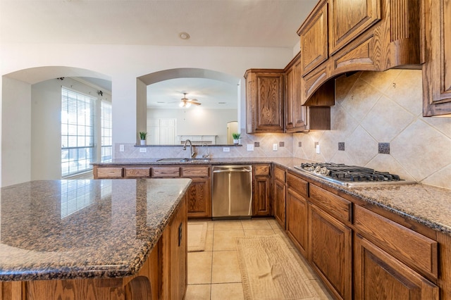 1364 Aubrey Ln, Frisco, TX 75033 - kitchen with appliances with stainless steel finishes, a sink, brown cabinetry, arched walkways, and backsplash